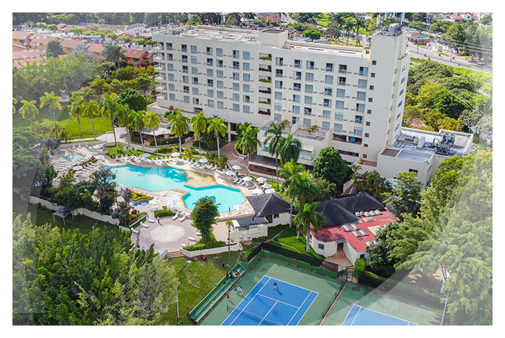 Vista aérea del hotel con piscina central, canchas deportivas y amplias zonas verdes, todo rodeado de naturaleza, ideal para disfrutar de las reservas en el hotel Altamira con descuento
