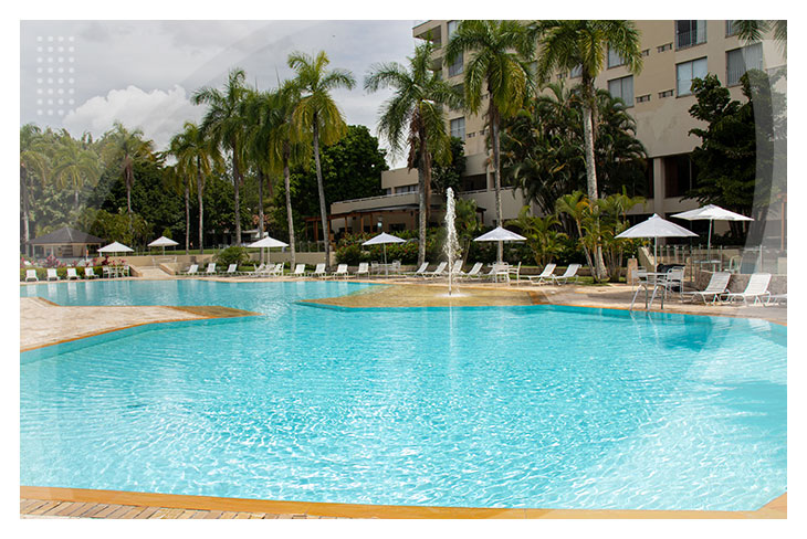 Piscina de agua cristalina rodeada de palmeras y sillas blancas con sombrillas, ofreciendo un ambiente tropical ideal para disfrutar de las reservas en el hotel Altamira con descuento
