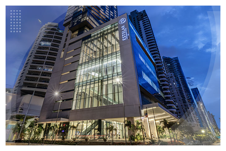 Edificio moderno con fachada de vidrio e iluminación nocturna, rodeado de rascacielos y palmeras, que hace parte del Hotel y centro de convenciones Estelar Cartagena