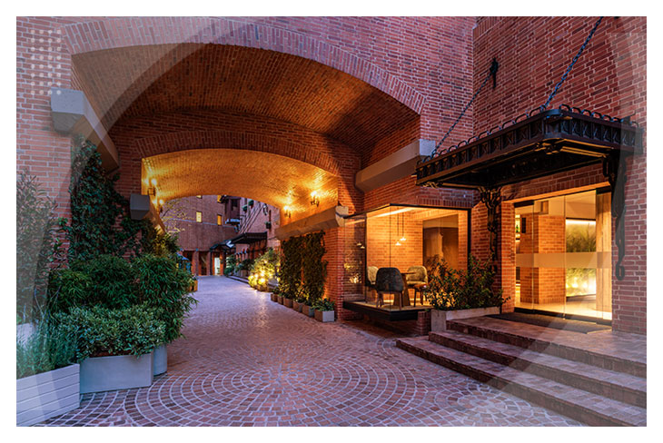 Camino con piso de piedra, rodeado de plantas con arcos de ladrillo e iluminación cálida que atraviesa una zona acogedora del Hotel Estelar La Fontana