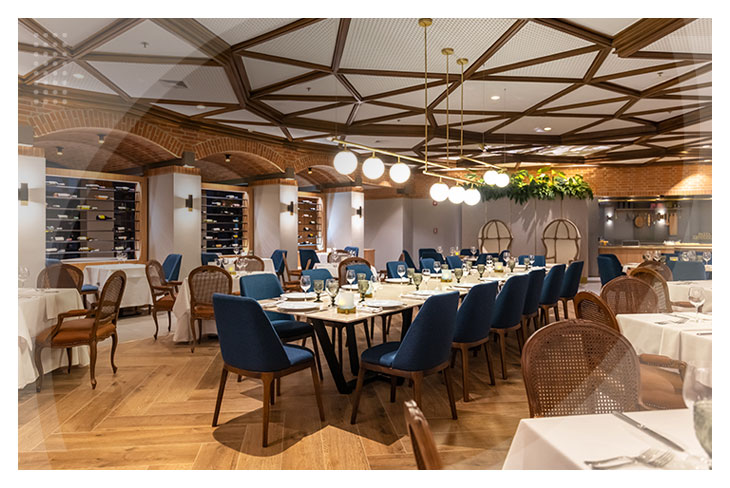 Restaurante elegante con varias mesas, sillas azules y marrones, iluminación cálida y techo de madera, en uno de los espacios que hacen parte de los restaurantes del Hotel La Fontana