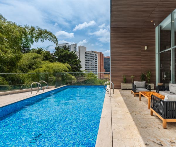 Piscina moderna que está ubicada en medio de una terraza, que tiene sofás para descansar, desde donde se puede ver la ciudad y disfrutar de una variedad de planes turísticos de Compensar y  Hoteles Estelar