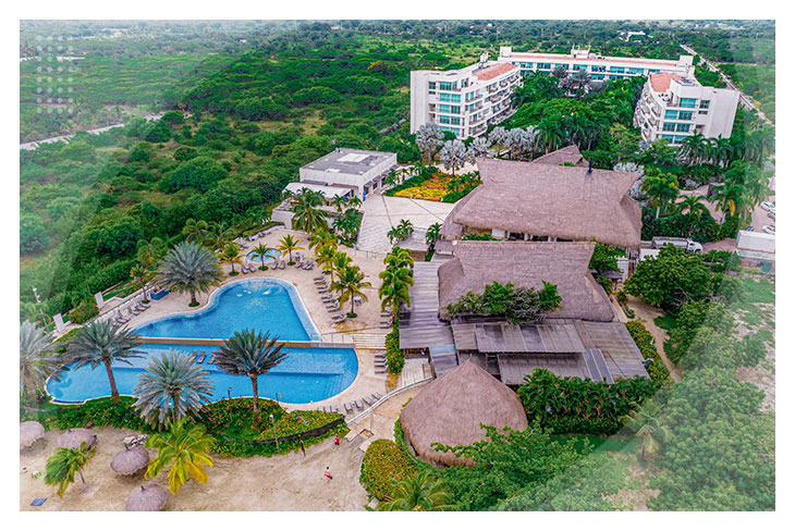 Vista aérea de un hotel rodeado de árboles con piscina azul, palmeras y techos en palma, una opción perfecta entre los mejores hoteles para hacer reservas en Cartagena