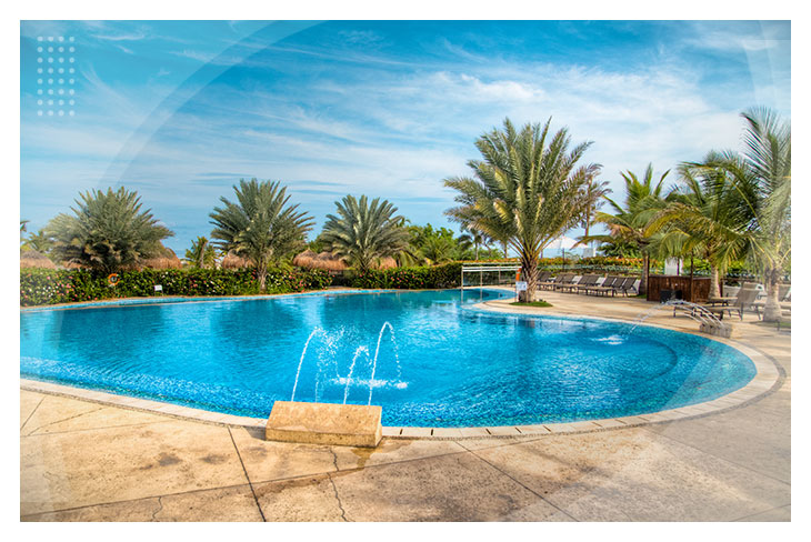 Piscina grande con chorros de agua, rodeada de palmeras bajo un cielo azul, perfecta para disfrutar en hoteles cerca a la playa Manzanillo