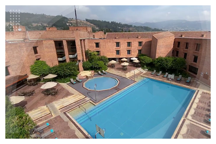 Piscina amplia con jacuzzi rodeada de sillas asoleadoras y sombrillas en un entorno natural con montañas de fondo en el hotel Estelar Paipa