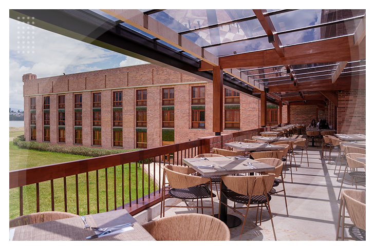 Zona de restaurante con techo de vidrio, múltiples mesas en una terraza con vista a zonas verdes en los hospedajes en Paipa al mejor precio