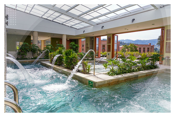 Zona de hidroterapia con caídas de agua y vegetación natural dentro de una piscina techada con vista a un paisaje montañoso en uno de los mejores hoteles en Boyacá