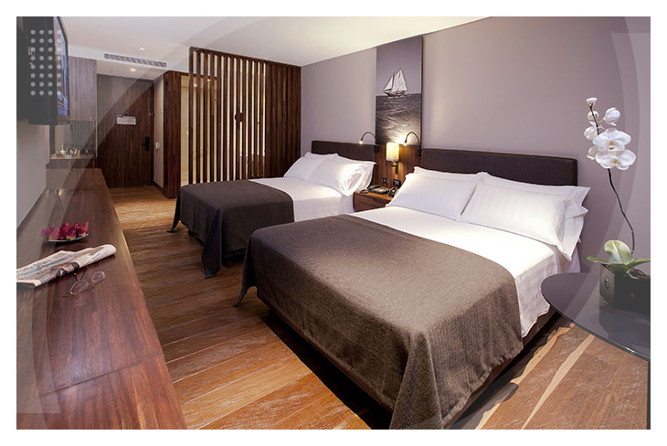 Habitación doble con piso en madera, dos camas amplias con sábanas blancas, iluminación cálida y detalles decorativos modernos, ideal para quienes buscan reservas en el hotel del parque de la 93 con descuento