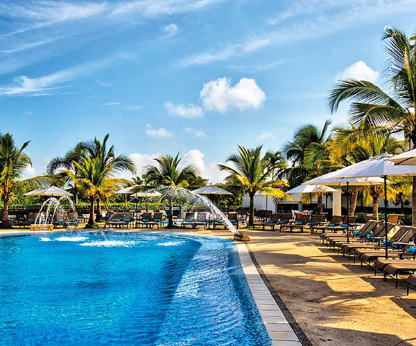 Piscina de agua cristalina que está rodeada de palmeras, sillas asoleadoras y parasoles blancos, está una de las locaciones que hace parte de la oferta de Hoteles Estelar en Colombia