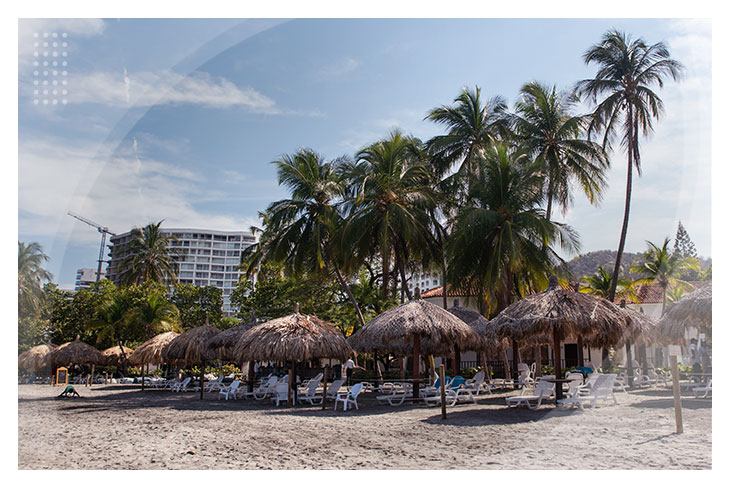 Playa amplia con quioscos de palma, sillas blancas y palmeras altas, perfecta para relajarse y disfrutar del ambiente tranquilo del Hotel Estelar Santamar