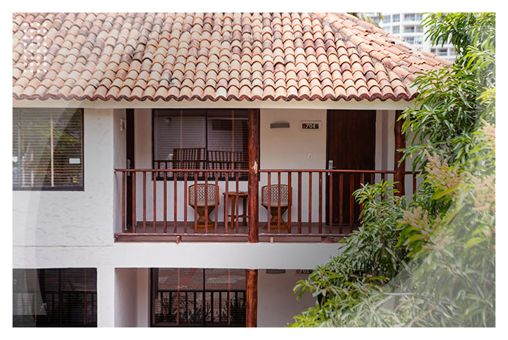 Balcón con sillas y mesa de madera frente a una habitación rodeada de árboles, en un ambiente tranquilo que hace parte de los hoteles Estelar en Santa Marta