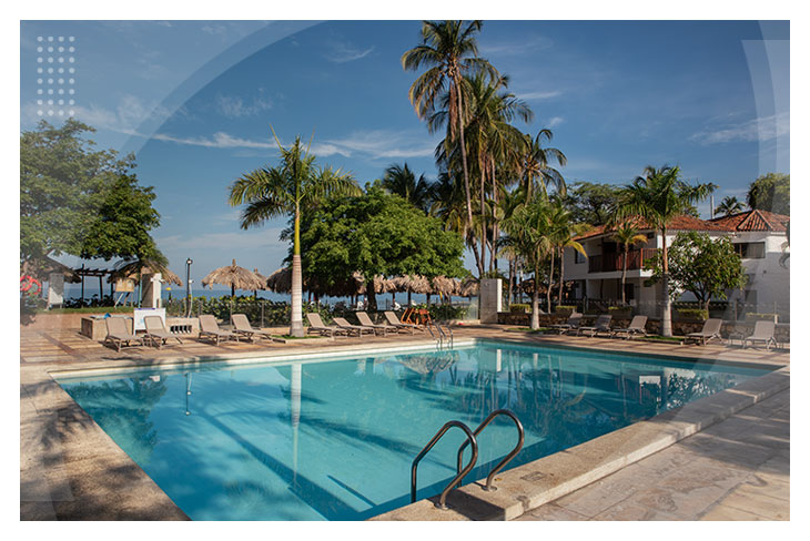 Piscina con sillas asoleadoras rodeada de palmeras y zonas verdes ideal para descansar y disfrutar en uno de los hoteles en Santa Marta cerca al mar