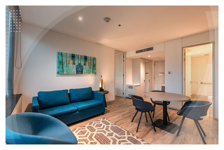 Ambiente moderno con sofá y sillas azules, mesa redonda y acceso a baño privado, disponible dentro de las reservas en el Hotel Estelar Square con una oferta especial