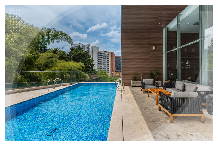 Piscina moderna al aire libre rodeada de naturaleza y un área de descanso que cuenta con múltiples sofás con vista a la ciudad, ideal para disfrutar de los distintos paquetes de viajes para ir a Medellín