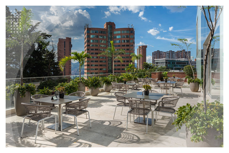 Terraza al aire libre con sillas y mesas rodeadas de naturaleza para compartir una gran vista de la ciudad y disfrutar de los mejores planes vacacionales todo incluido en Medellín
