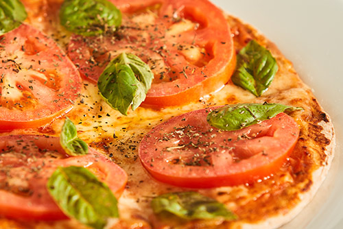 Pizza napolitana con salsa de tomate, queso, tomate en rodajas, hojas de albahaca y especias, sobre un plato blanco