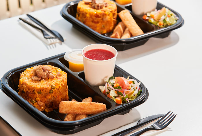 Dos platos de color negro que tienen en su interior arroz con pollo, yuca, ensalada, salsa y jugo de mora, están sobre una mesa de color blanco ubicada en una de las locaciones a las cuales se puede acceder al hacer una reserva en Lagosol Compensar