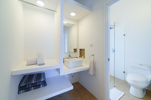 Baño moderno de las habitaciones en el centro vacacional Las Palmeras, donde se puede encontrar un diseño de compartimientos que muestra un armario y el lavamanos junto a una pared transparente que conecta con el retrete