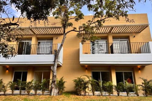 Dos casas color beige con balcones blancos de las tarifas especiales del centro vacacional Las Palmeras, con árboles y plantas pequeñas en el patio que rodea las instalaciones