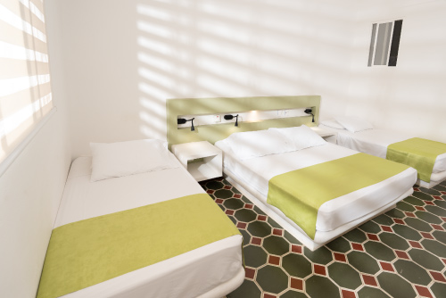 Habitación con descuento del hotel Las Palmeras con un piso de baldosas simétricas con tres camas, dos dobles y una personal, con una mesa de noche, un televisor y una ventana
