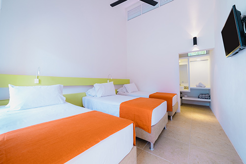 Habitación del centro vacacional Las Palmeras  con tres camas personales, un closet amplio, un televisor y un ventilador