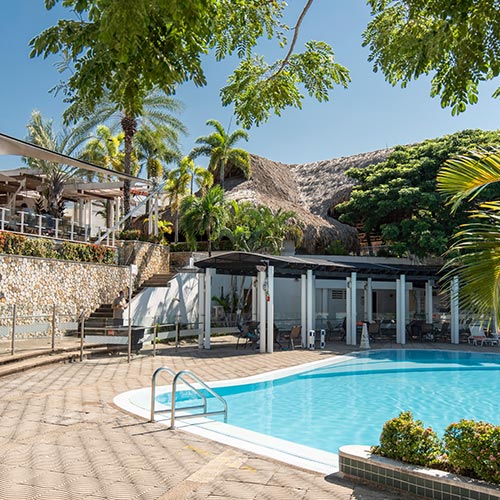 Piscina con agua cristalina, rodeada de sillas asoleadoras que tienen un techo que las cubre. Subiendo las escaleras hay un gran kiosko con techo de paja, en donde se pueden hacer las reservas del hotel Lagomar días festivos. Alrededor hay árboles y palmeras