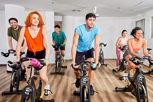 Gimnasio en donde se encuentran seis personas, tres hombres y tres mujeres, ejercitándose en elípticas y disfrutando de los planes en Lagomar
