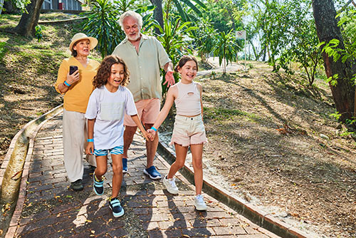 Hombre y mujer adultos, caminan con  dos niños por un sendero natural en un  lugar con clima cálido. Aprovechando los beneficios de hacer reservas en el hotel Compensar entre semana