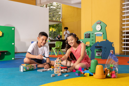 Un niño y una niña jugando Jenga dentro de un salón con un piso de color azul, amarillo, rojo, celeste y que tiene algunos juegos de niños, los cuales hacen parte de la oferta de los planes en el hotel Lagosol
