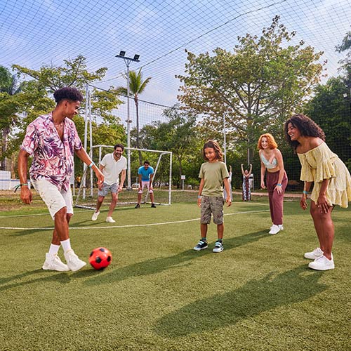 Familia de seis personas jugando un partido de fútbol en una cancha sintética  ubicada en medio de la naturaleza, la cual hace parte de una de las actividades en Lagomar durante la temporada alta