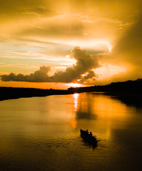 Pequeña canoa navegando por el río Amazonas al atardecer, con el cielo dorado reflejado sobre el agua tranquila