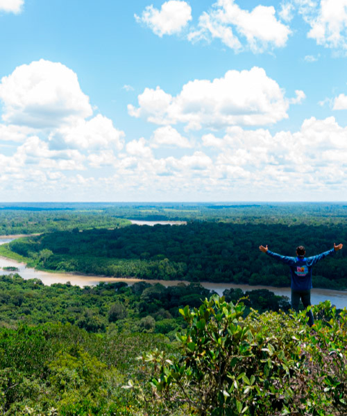 Hombre, con los brazos extendidos hacia los lados, contemplando la selva y los ríos desde un mirador natural, el cual hace parte del paquete turístico Guaviare con visita a los miradores