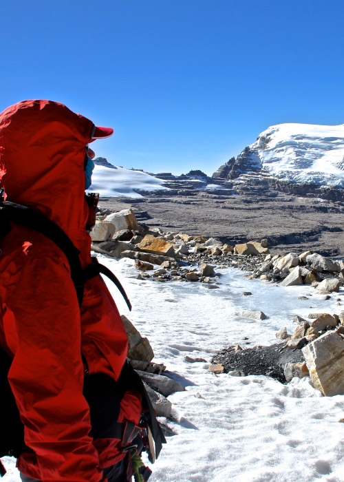 Persona, que usa chaqueta roja térmica, disfruta de la vista en Parque Nacional Natural el Cocuy, que es considerado como uno de los mejores lugares para hacer ecoturismo en Colombia con Compensar